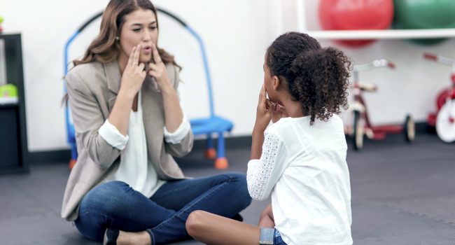 Adult female therapist guiding young girl in speech therapy for a therapy exercise